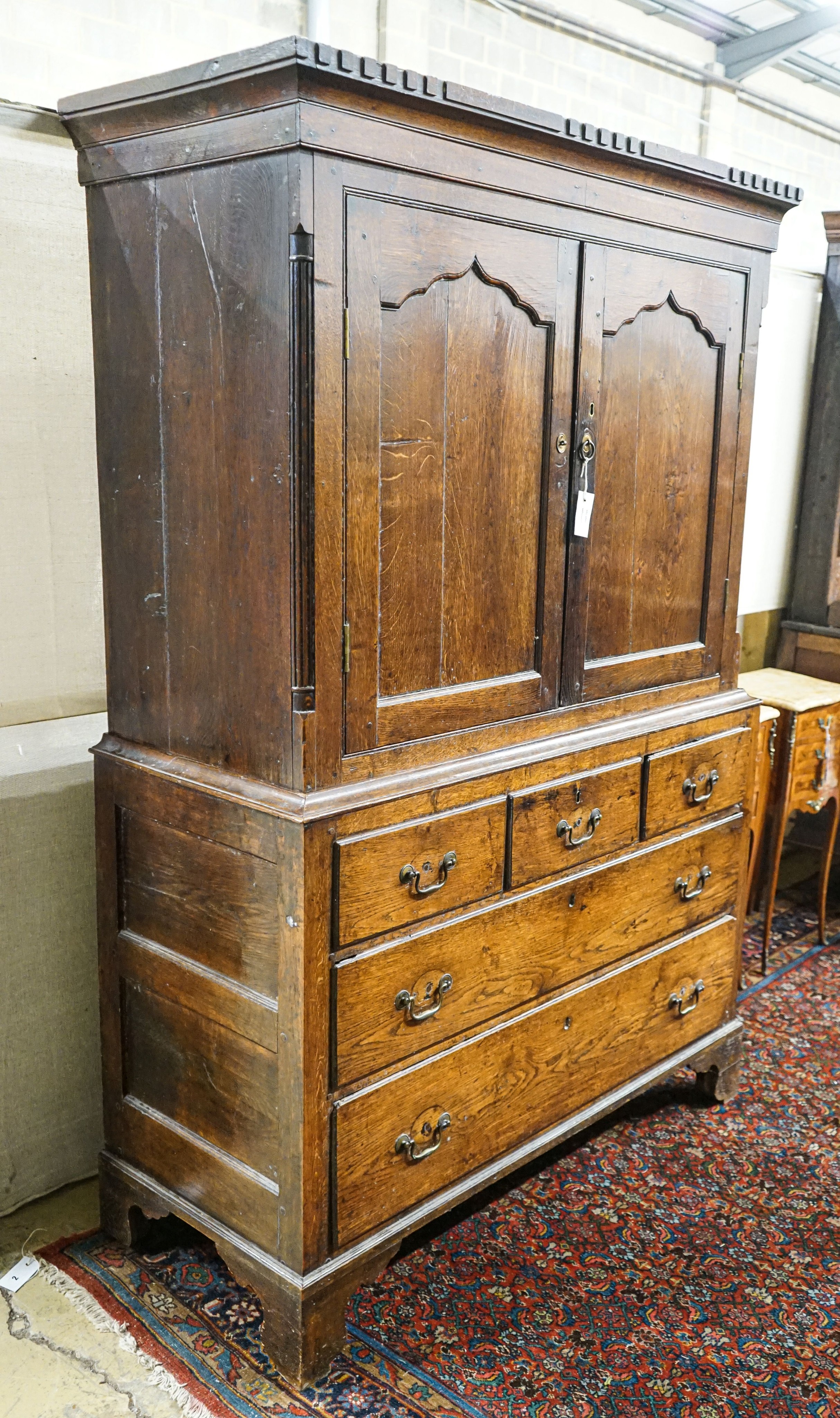A George III oak press cupboard, with moulded cornice and two panelled doors over five drawers, width 122cm, depth 52cm, height 183cm